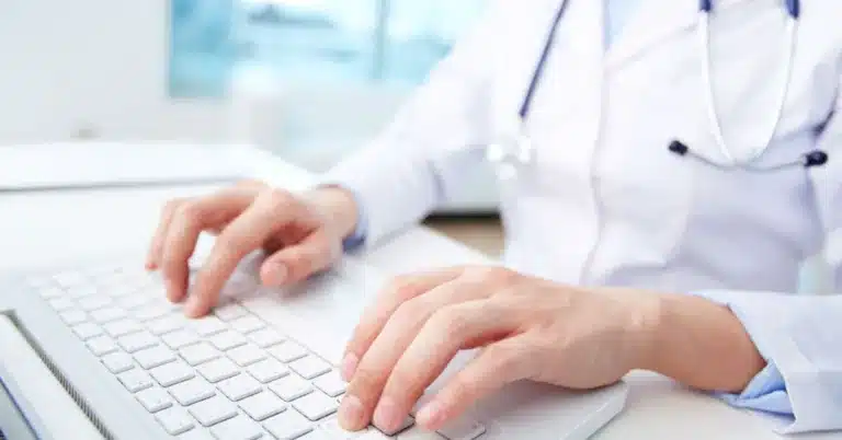 Healthcare worker typing on hospital laptop.